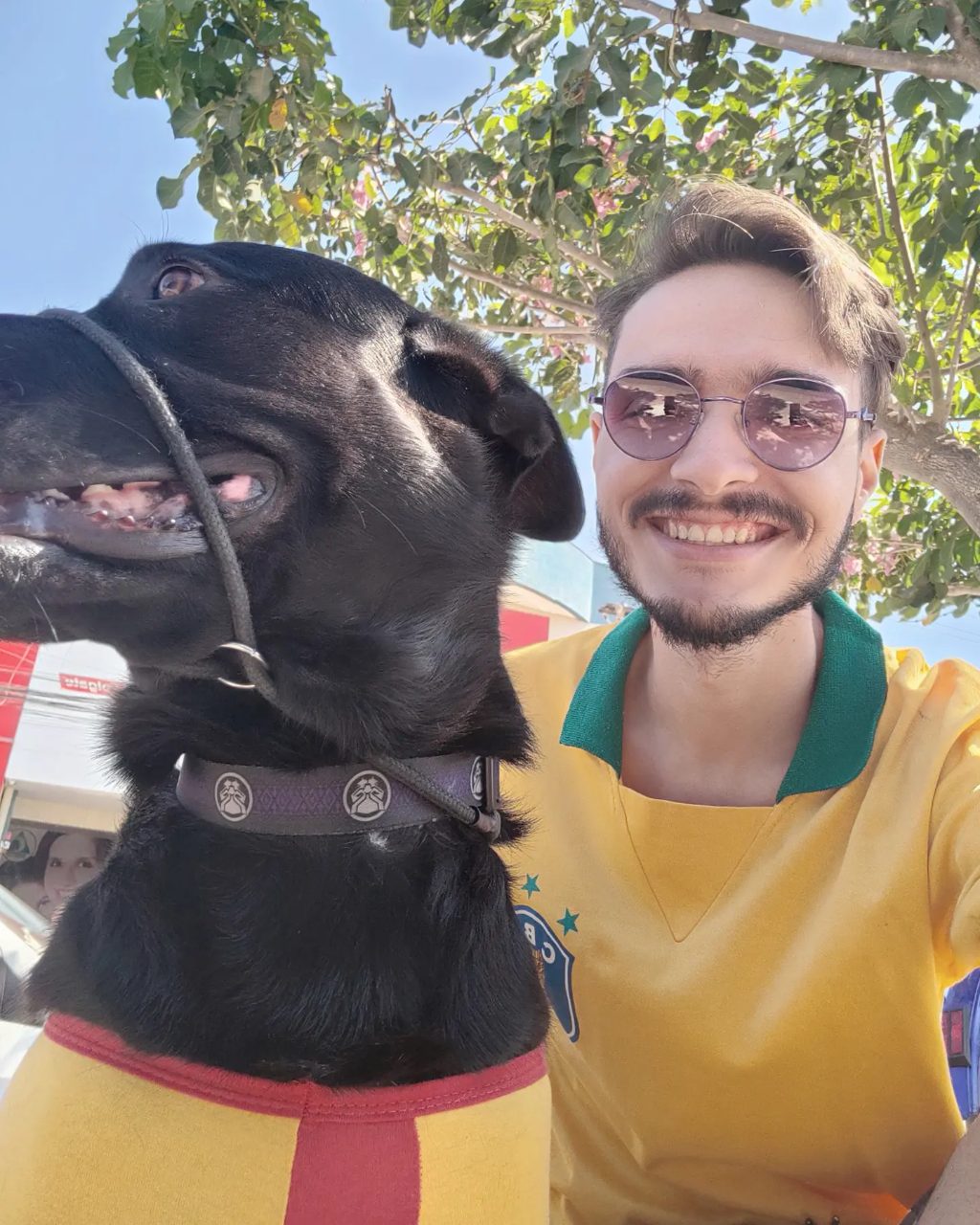 Matheus Ché sorrindo ao lado do seu cachorro preto, Apolo