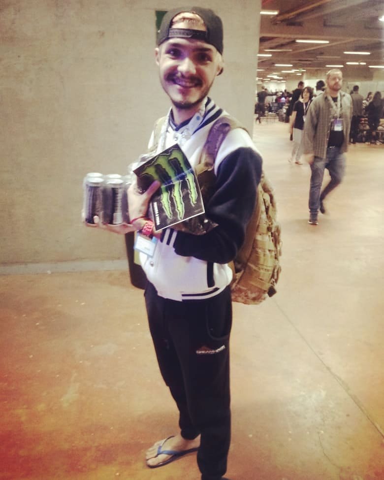 Matheus Ché na Campus Party Brasília segurando a camisa e o pack de energéticos que ganhou no desafio da Monster Energy