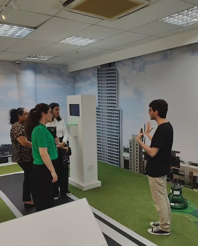 Matheus Ché apresentando para um grupo diante de uma maquete com pista e prédios
