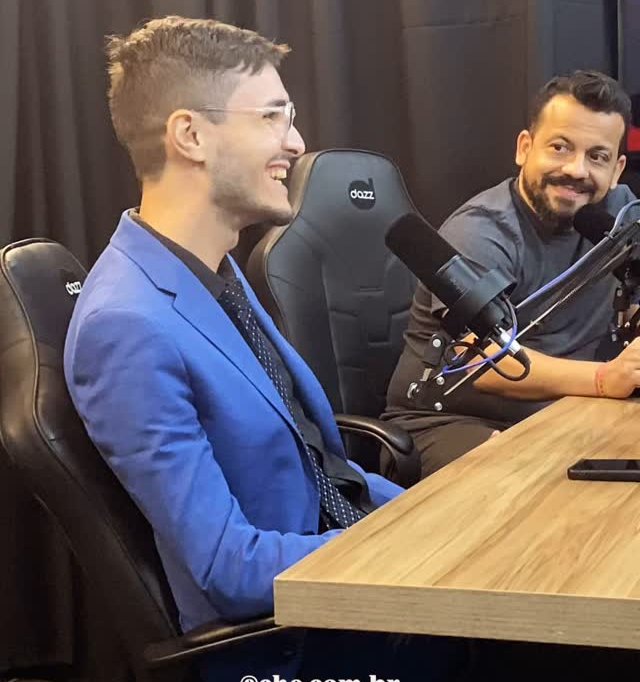 Matheus Ché, de blazer azul, falando ao microfone no estúdio do Podcast Daquele Jeito