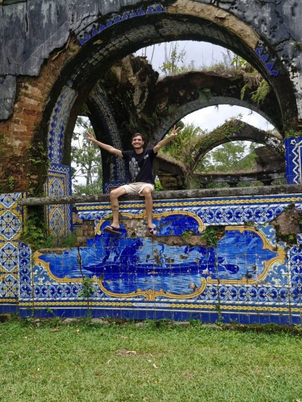 Matheus Ché sentado sob arcos decorados com azulejos azuis