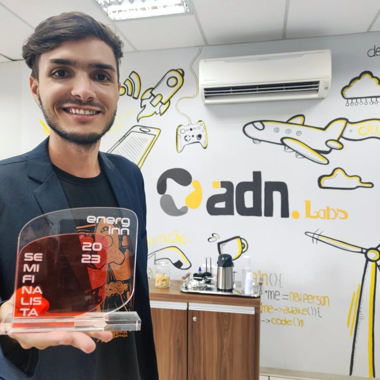 Matheus Ché segurando o troféu de semifinalista do EnergINN 2023 no escritório da ADN.tech